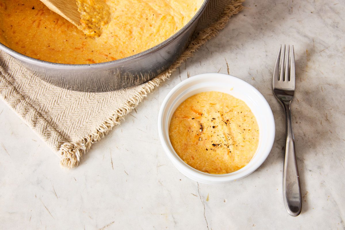 small bowl of cheese grits on counter with fork with pot of grits in background