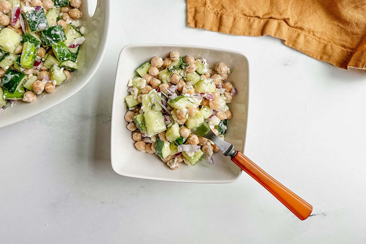 Taste of Home chickpea cucumber salad in white ceramic bowls with linen napkin on a marble surface.