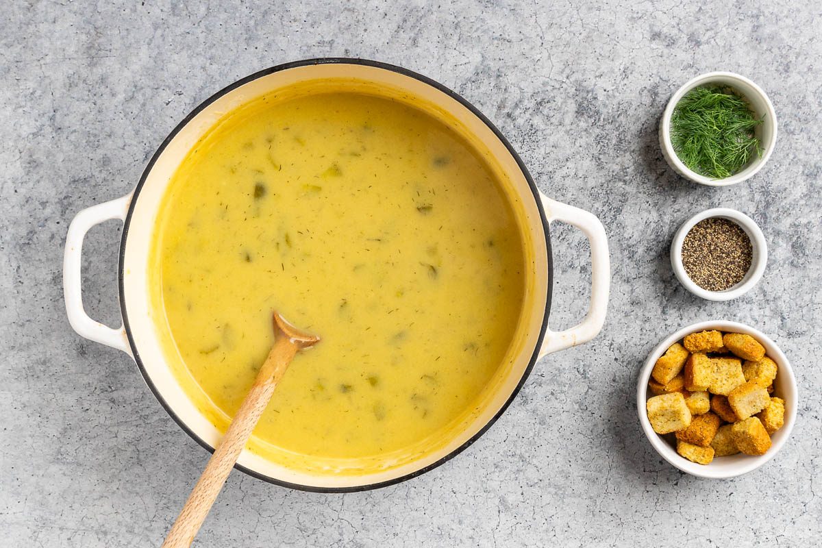 Taste of Home Dill Pickle Soup recipe photo of the milk added to the soup with fresh dill, fresh cracked pepper and croutons for garnish.