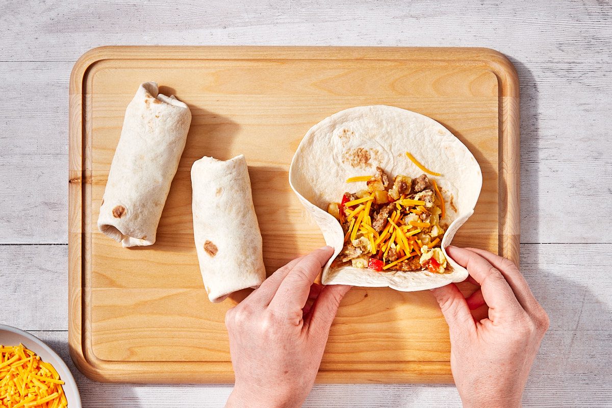 Freezer Breakfast Burritos Step 2- rolling filled tortillas on cutting board