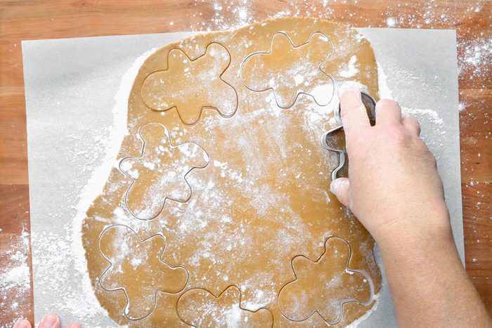 A hand is visible pressing the gingerbread man cookie cutter into the gingerbread dough.
