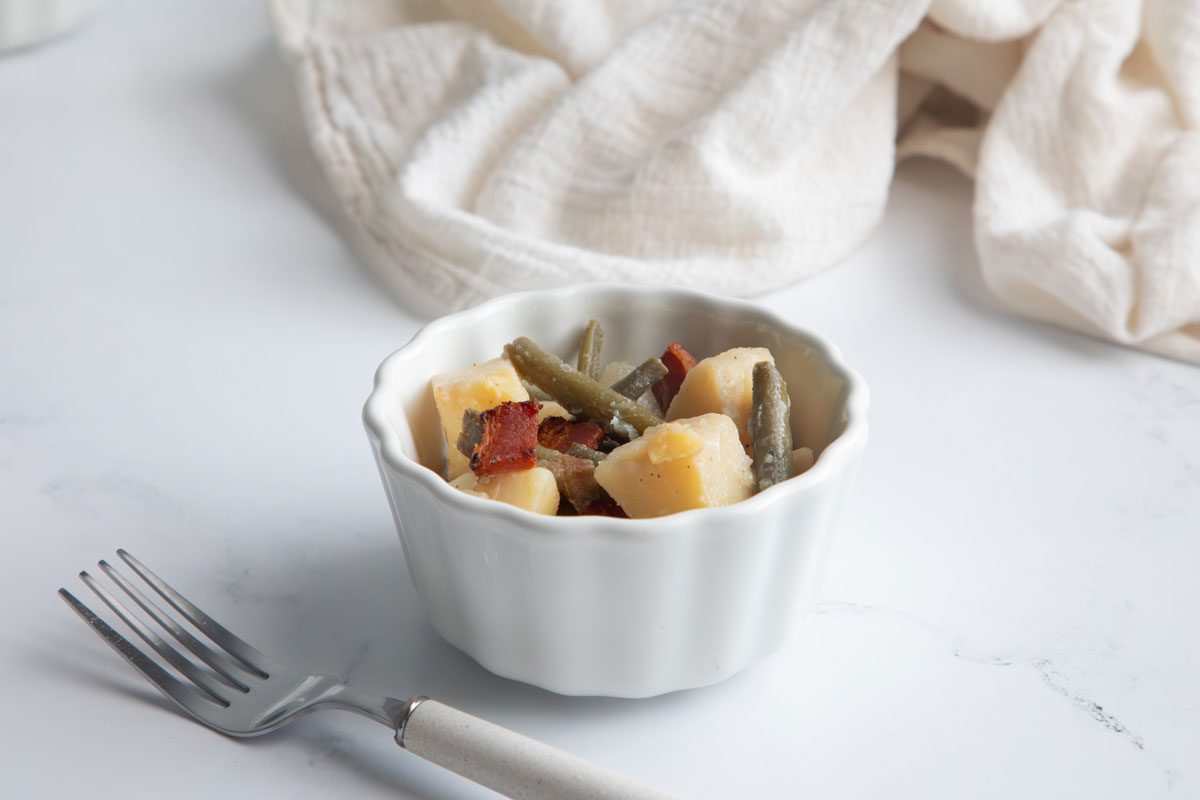 Horizontal beauty shot for Taste of home green beans and potatoes in small bowl with fork on a marble surface.