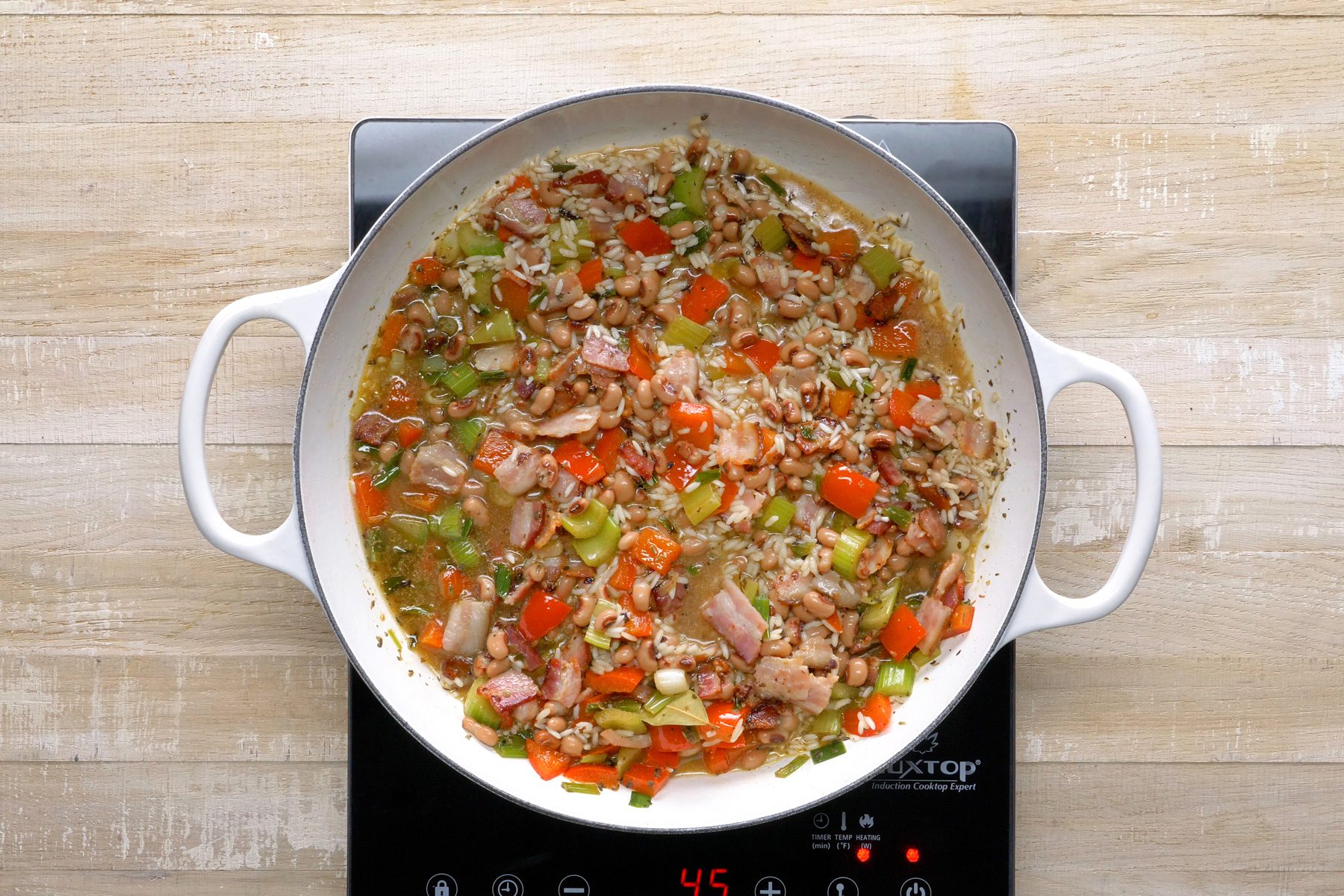 Top view shot of black eyed peas and bacon added to skillet