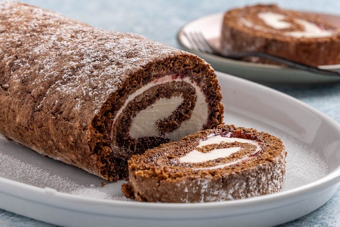 Taste of Home Ice Cream Cake Roll recipe photo the cake rolled up sprinkled with powdered sugar and sides of chocolate sauce and whipped cream.