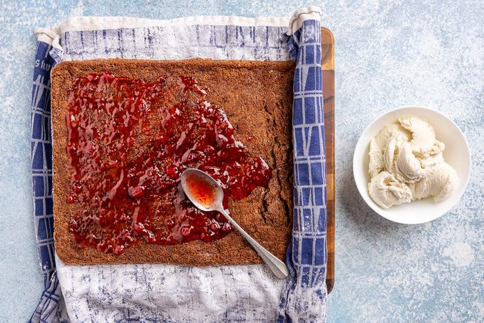 Taste of Home Ice Cream Cake Roll recipe photo of sheet cake unrolled and strawberry jam spread across with bowl of vanilla ice cream next to it.