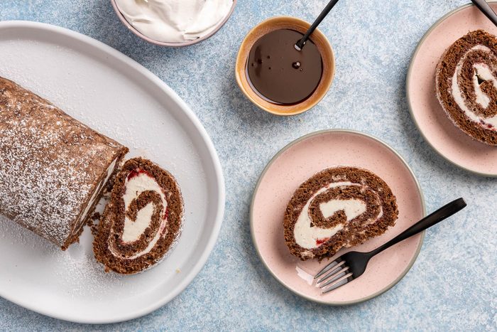 Taste of Home Ice Cream Cake Roll recipe photo the cake rolled up sprinkled with powdered sugar and sides of chocolate sauce and whipped cream.