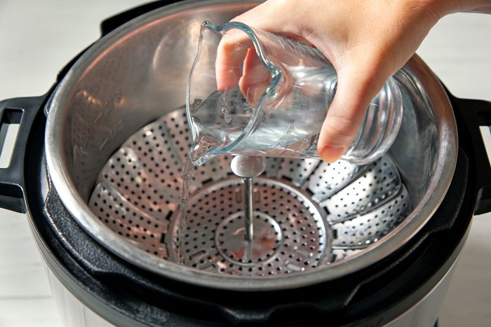 Hand pouring water in a steamer basket inside instant pot
