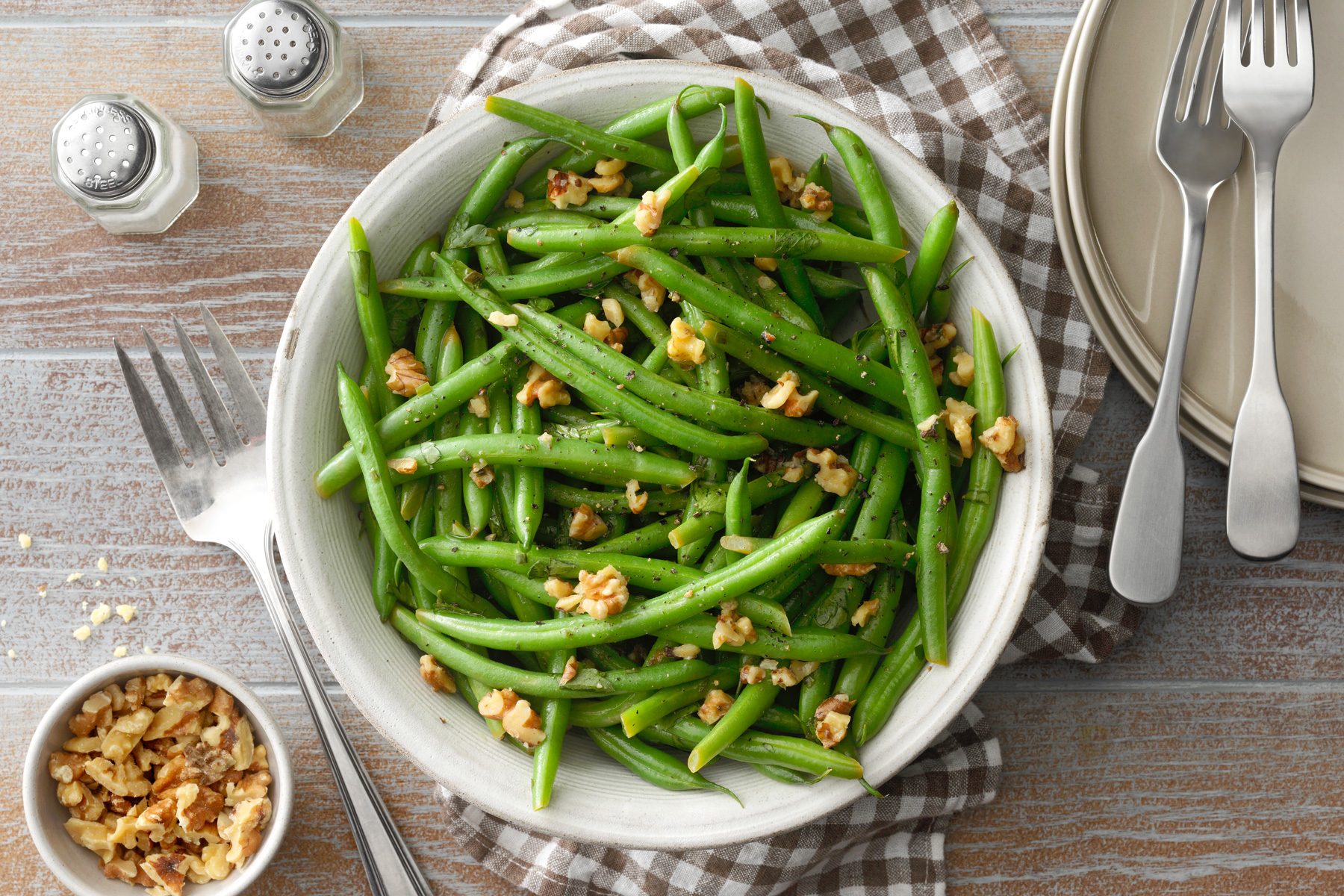 Top view shot of Instant Pot Green Beans served with walnuts on top and cutlery on side