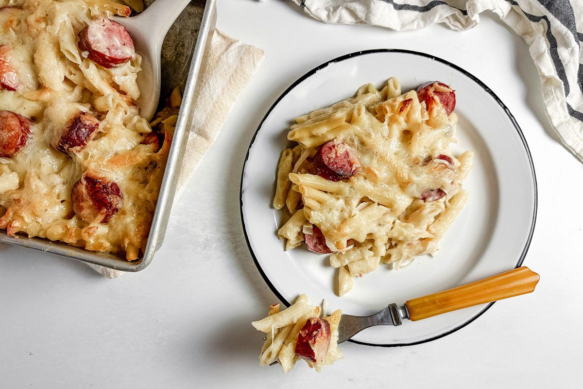 Taste of Home kielbasa casserole on an enamel plate next to a baking dish with kielbasa casserole.