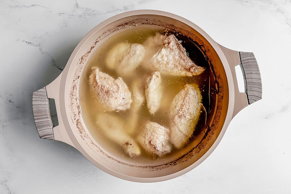 Poached chicken in a Dutch oven set on a marble surface for Taste of Home okra gumbo.