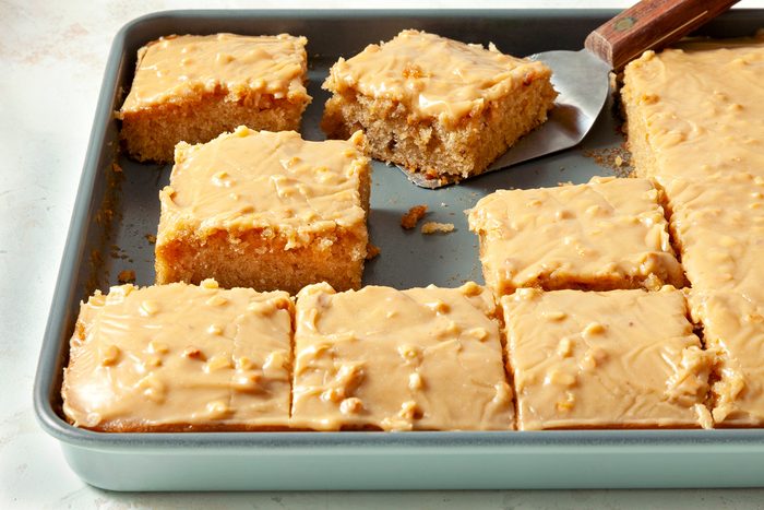 3/4th shot; horizontal; white textured background; Peanut Butter Sheet Cake cut into square pieces in baking tray;