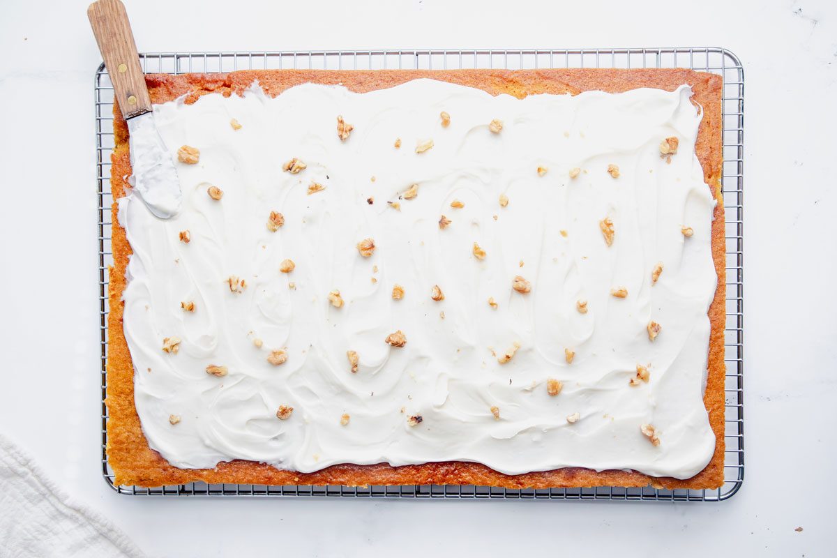 Overhead shot for Taste of Home Pumpkin Sheet Cake, cake cooling on a wire rack with frosting and walnuts on top.