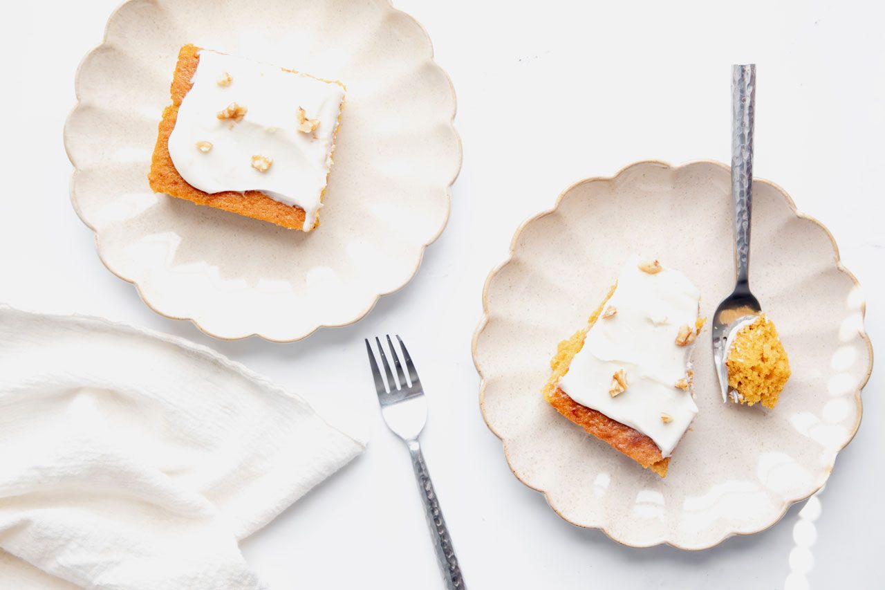 Overhead beauty shot for Taste of Home Pumpkin Sheet Cake on a marble surface with forks, walnuts, frosting, and linen.