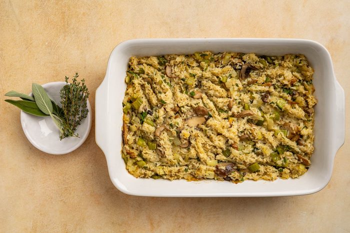 Taste of Home Rice Dressing recipe photo of the recipe cooked in a baking dish with a side of fresh sage and thyme for garnish.