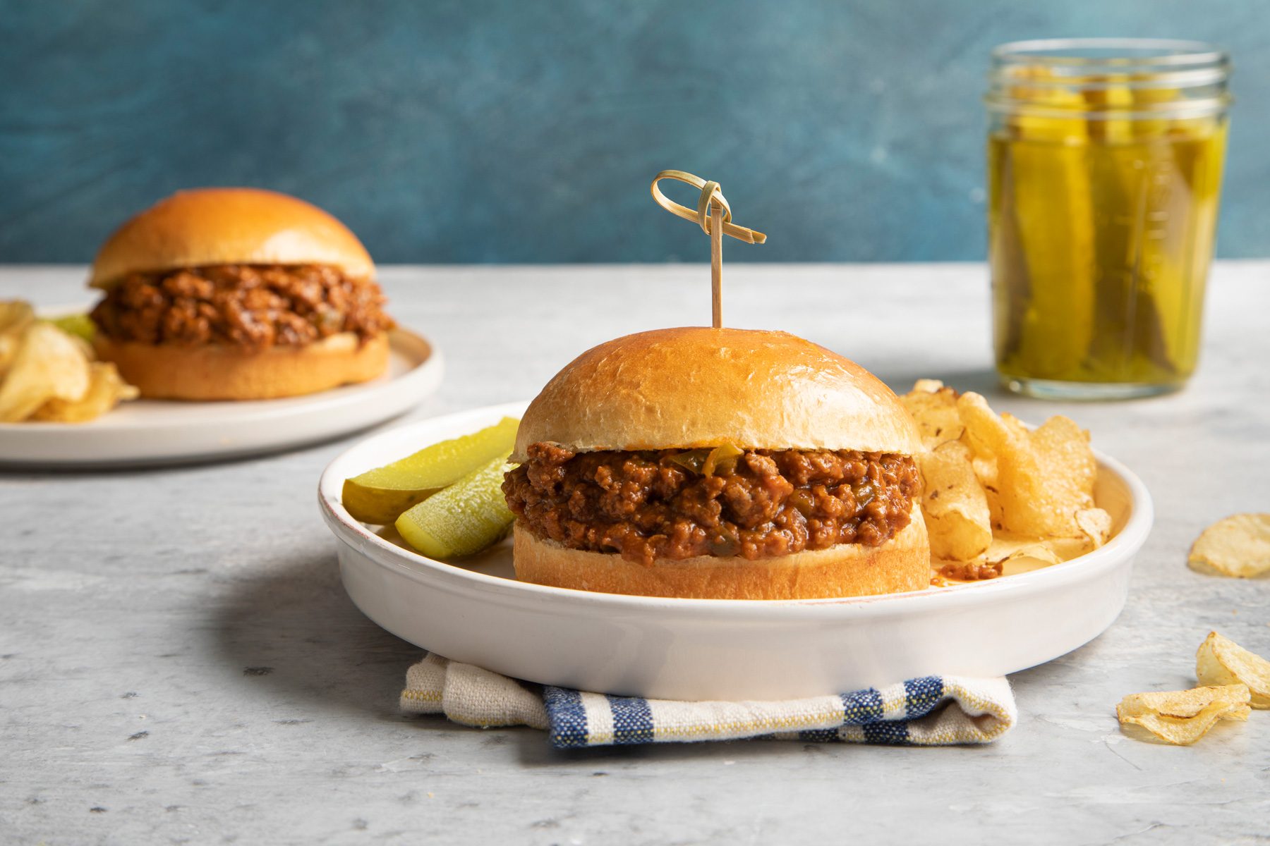 Slow Cooker Sloppy Joes burgers served on two plates with potato chips and pickle