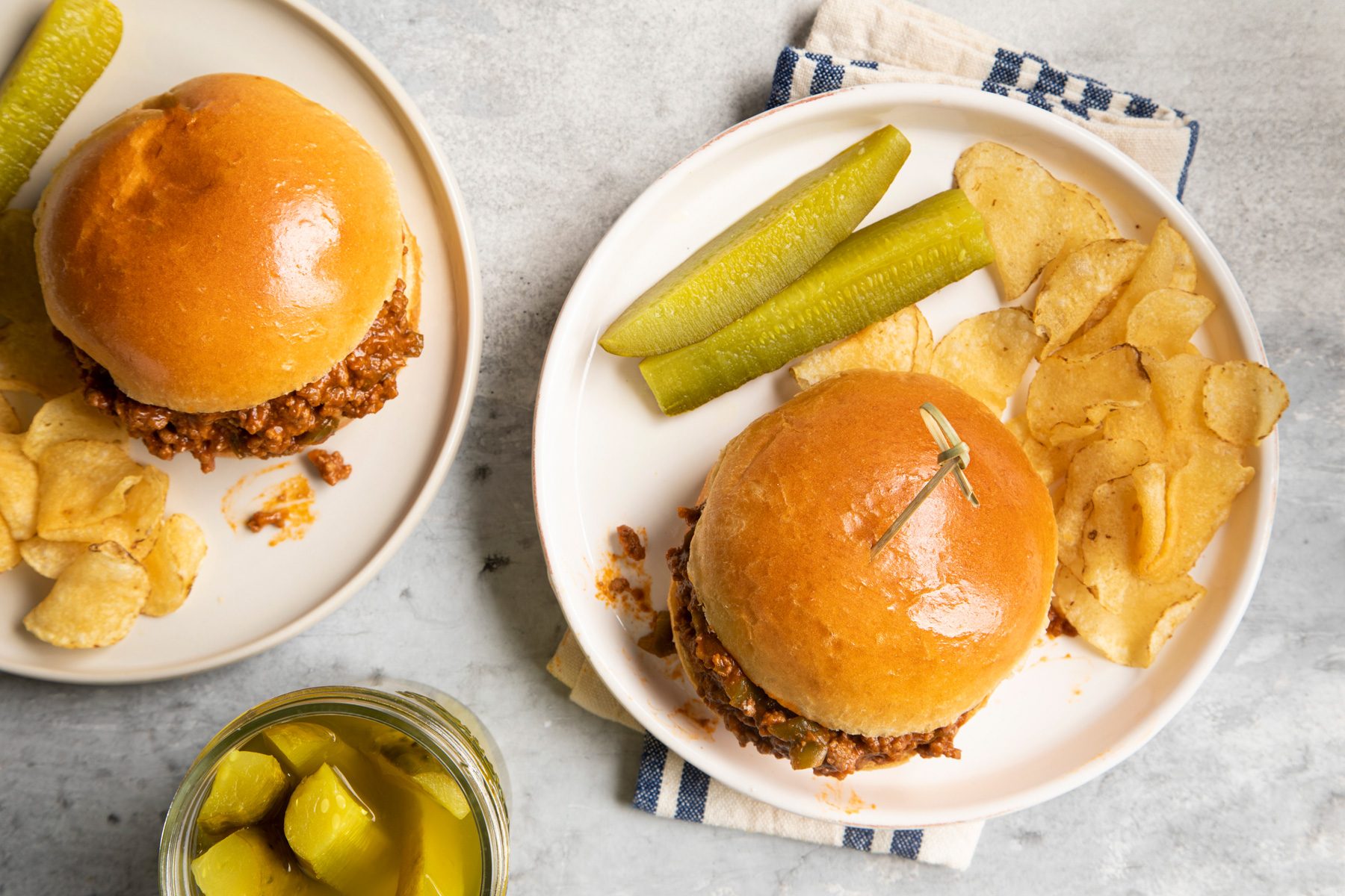 Top view of slow Cooker Sloppy Joes burgers served on two plates with potato chips and pickle