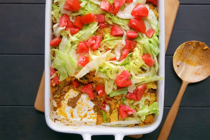 overhead shot; black background; Taco Casserole in a long baking dish placed over wooden board with woodeb serving spoon;