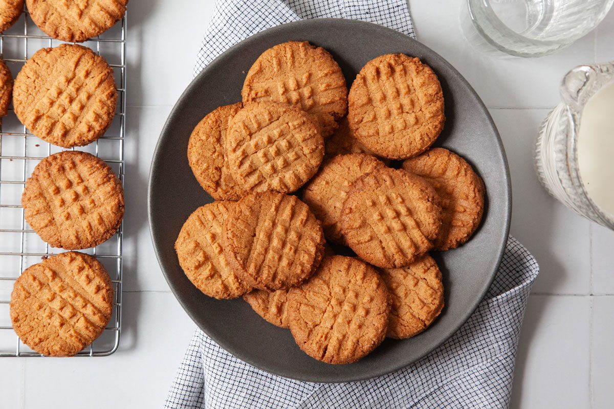Full yield of Taste of Home 3-Ingredient Peanut Butter Cookies on a black plate, milk glasses and pitcher