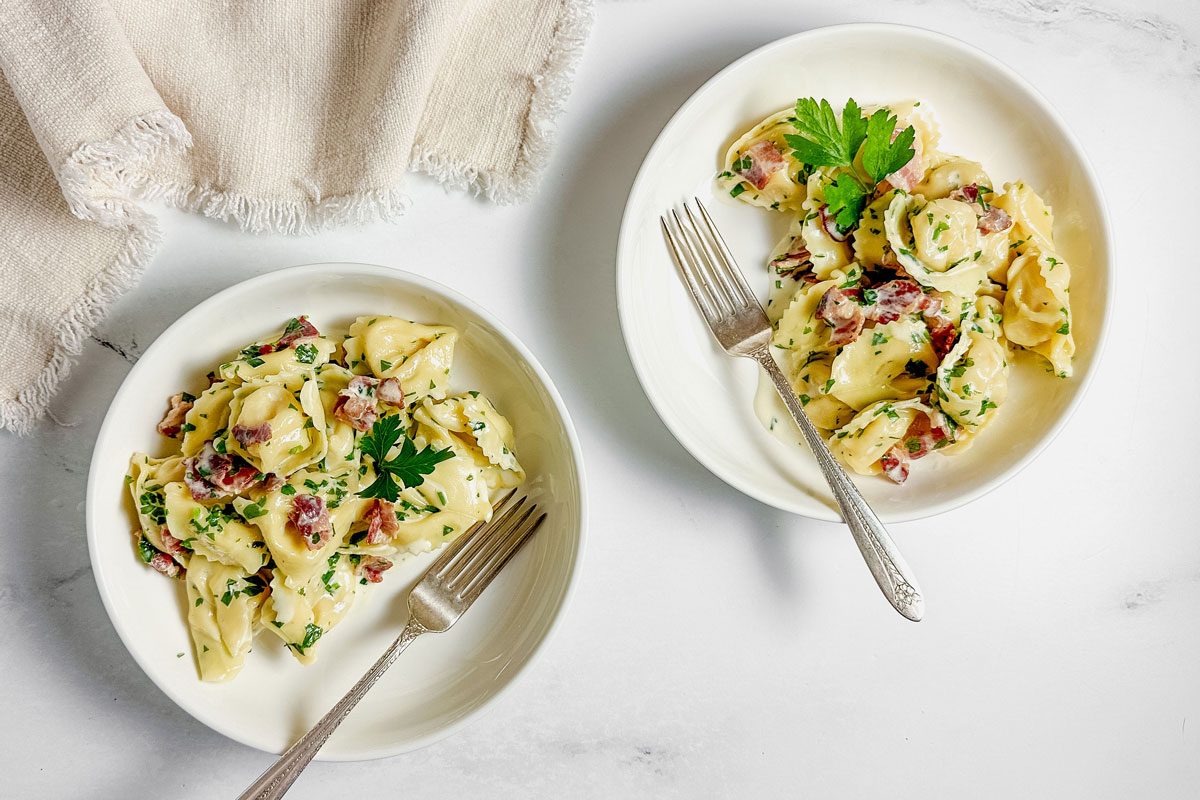 Taste of Home tortellini carbonara in white ceramic bowls with a linen napkin on a marble surface.