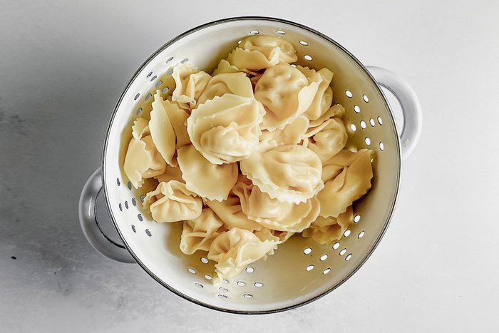 Cooked and drained tortellini in a white colander on a marble surface for Taste of Home tortellini carbonara.