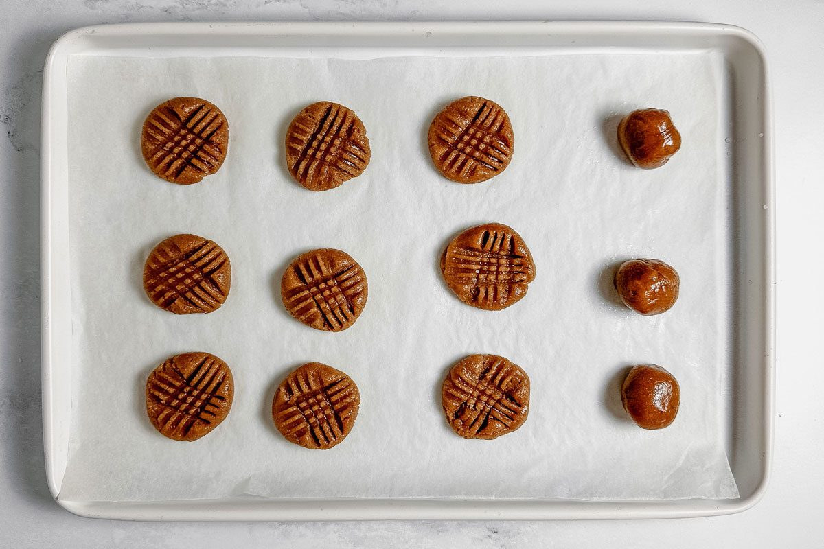 Unbaked Taste of Home vegan peanut butter cookies on a white baking sheet on a marble surface.