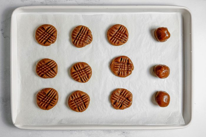 Unbaked Taste of Home vegan peanut butter cookies on a white baking sheet on a marble surface.