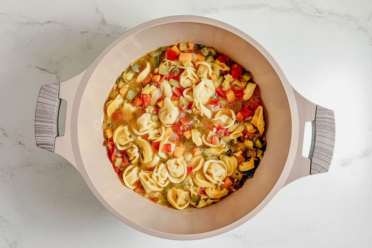 Taste of Home vegetarian tortellini soup in a Dutch oven on a marble surface.