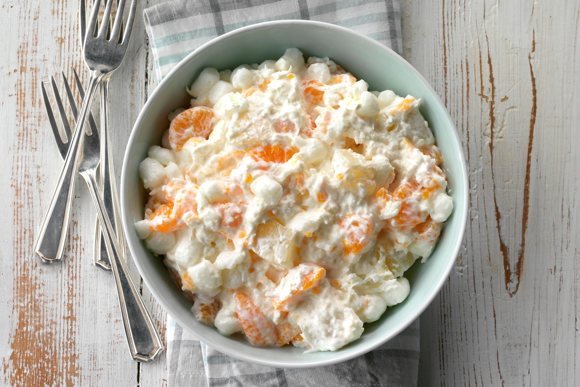 overhead shot of Ambrosia Salad in a large bowl; forks; kitchen napkin; wooden background;