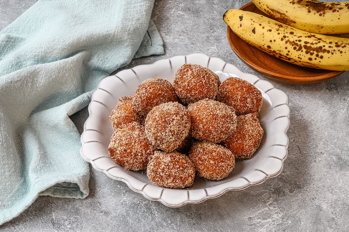 A bowl of banana beignets with bananas in the background.