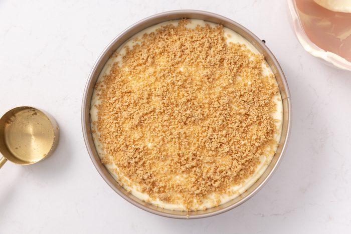 Banana cream cheesecake being finalized with crumbs topping.