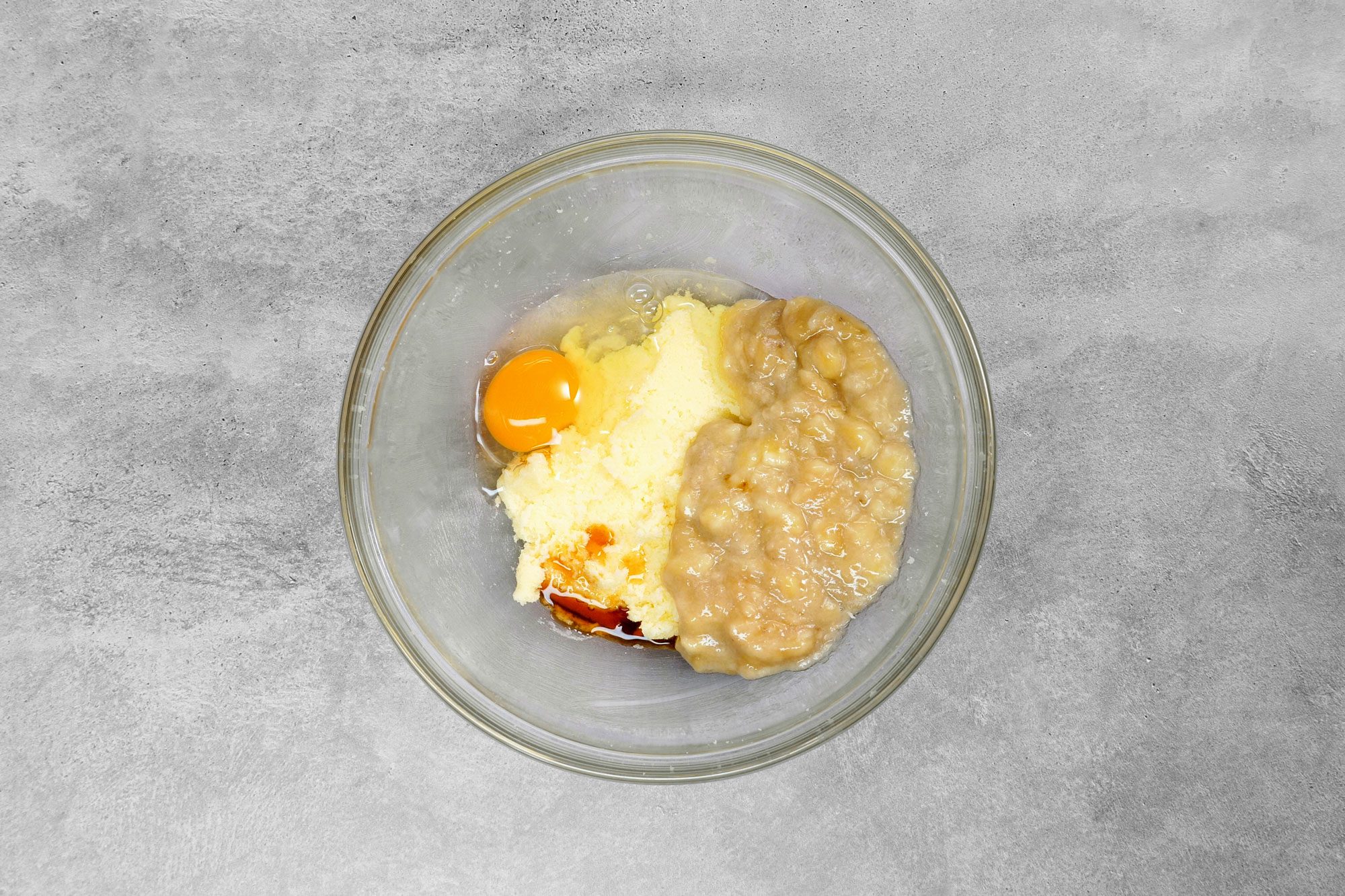 overhead shot; grey background; egg, beaten banana and vanilla in a small bowl;