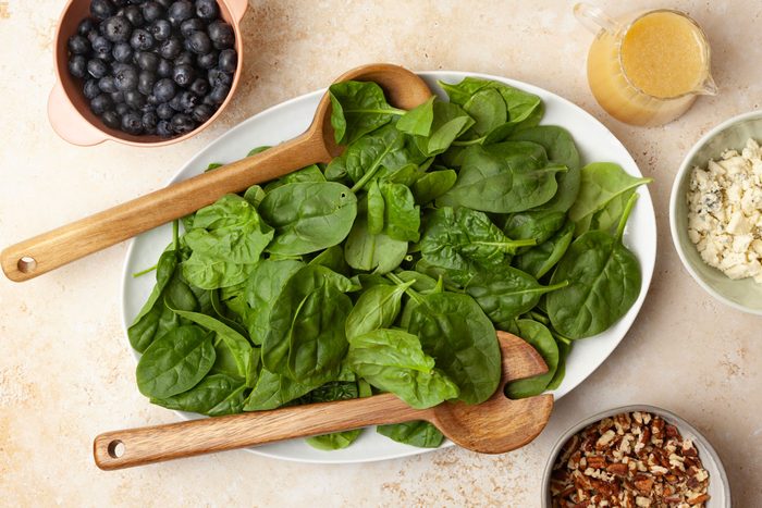 Step 2 of Taste of Home Blueberry Salad is to place the spinach, blueberries, blue cheese and pecans. Drizzle the dressing over the salad, and toss to combine.