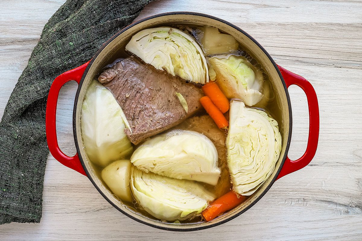 Boiled dinner preparation with corned beef, cabbage, potatoes, carrots, and onions.