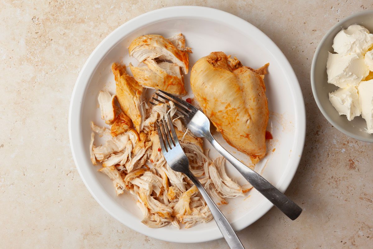 Step 2 of Taste of Home Buffalo Chicken Chili is to remove the chicken and shred it with a fork before returning it to the pan along with the cubed cream cheese