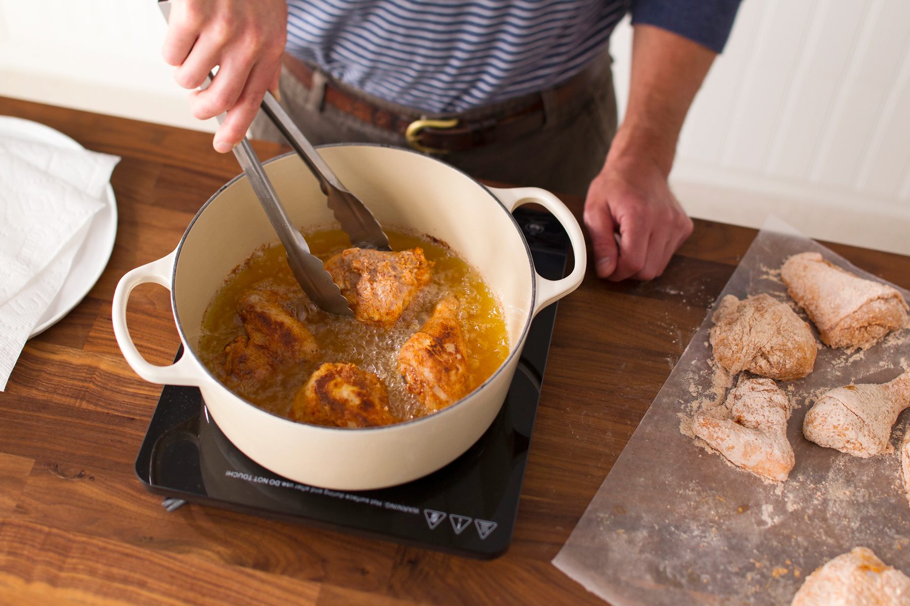 Person using metal tongs to fry the four pieces inside their dutch oven of hot, bubbling oil