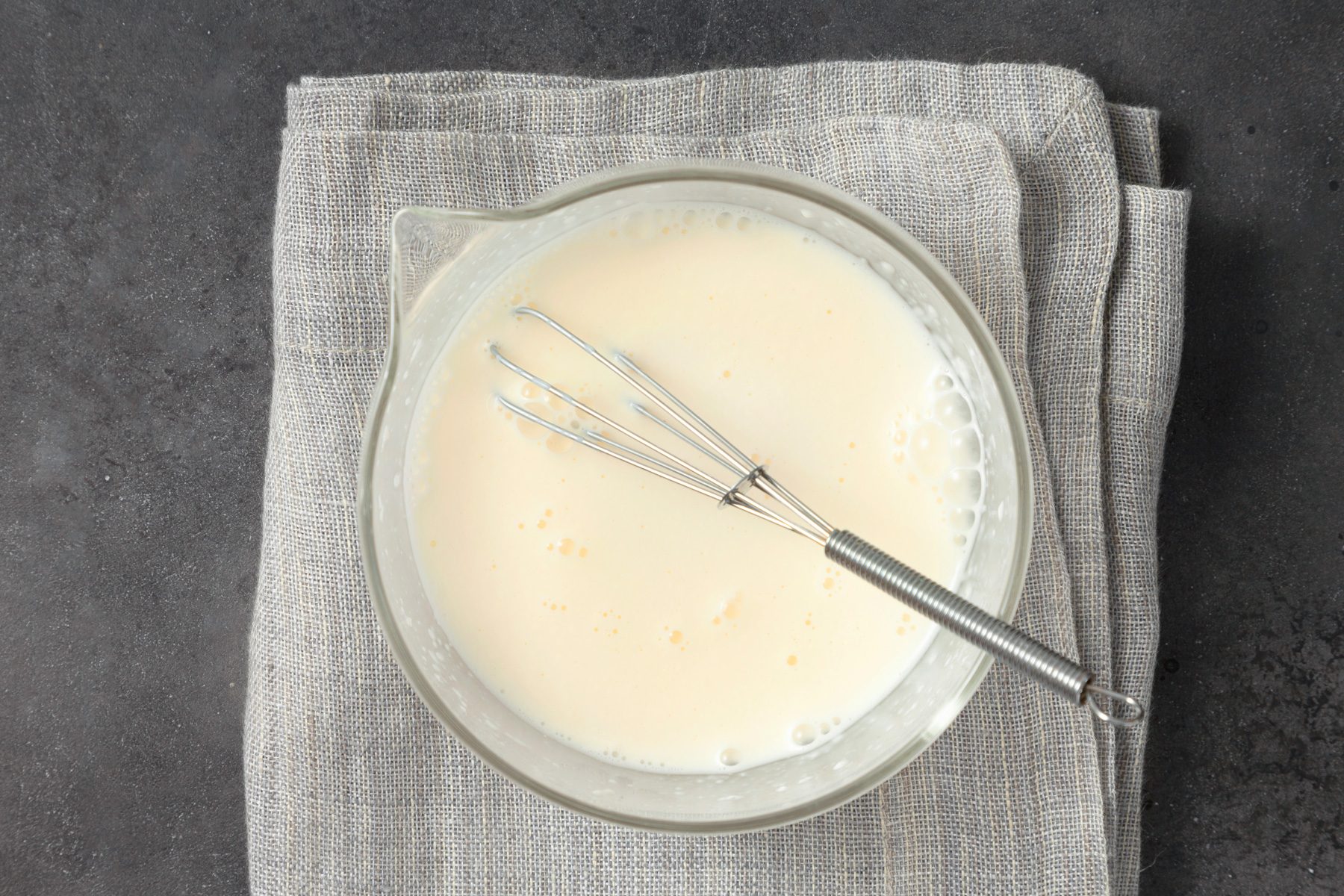 overhead shot; dark grey background; In a small bowl, placed over kitchen towel; combined mayonnaise, vinegar, sugar and salt; whisker is placed inside the bowl