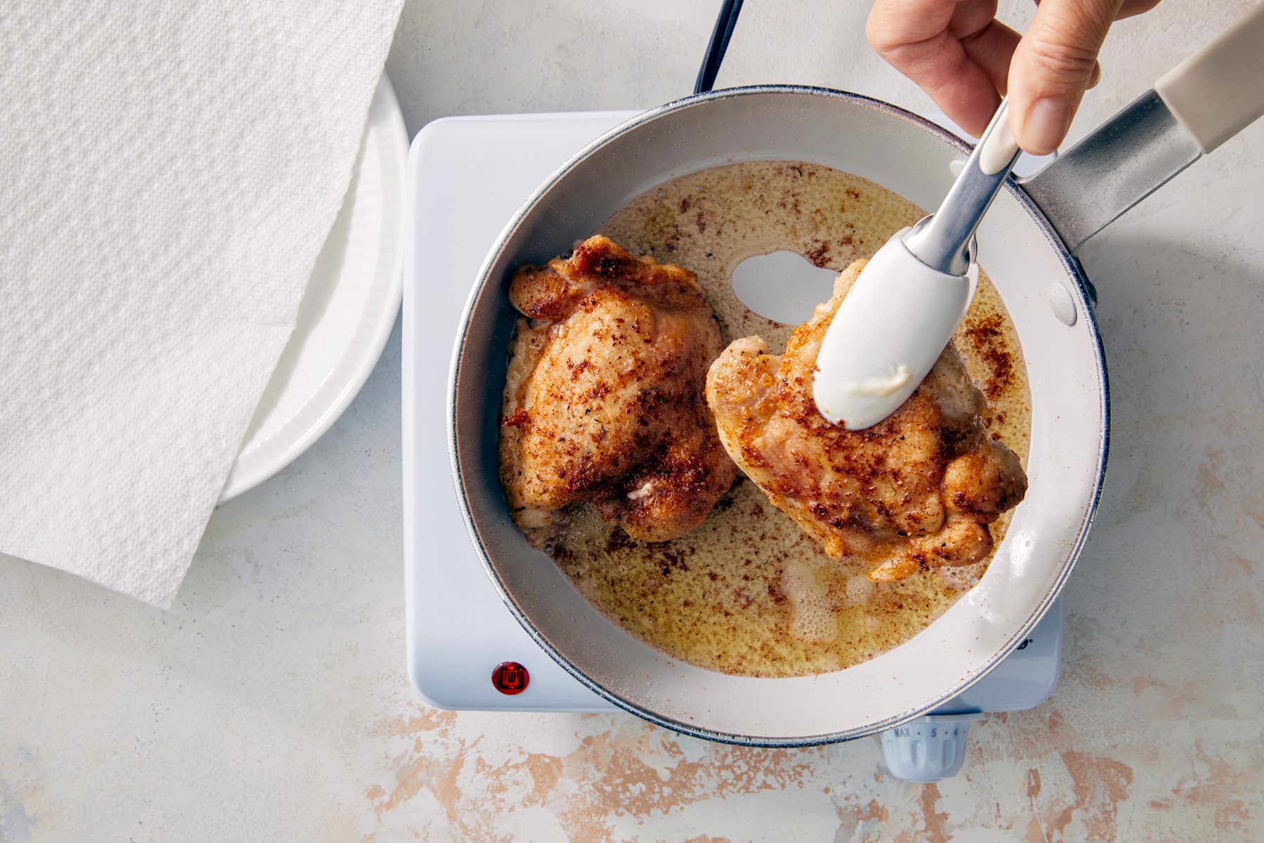 overhead shot; white textured background; Added oil to skillet and frying chicken until golden brown