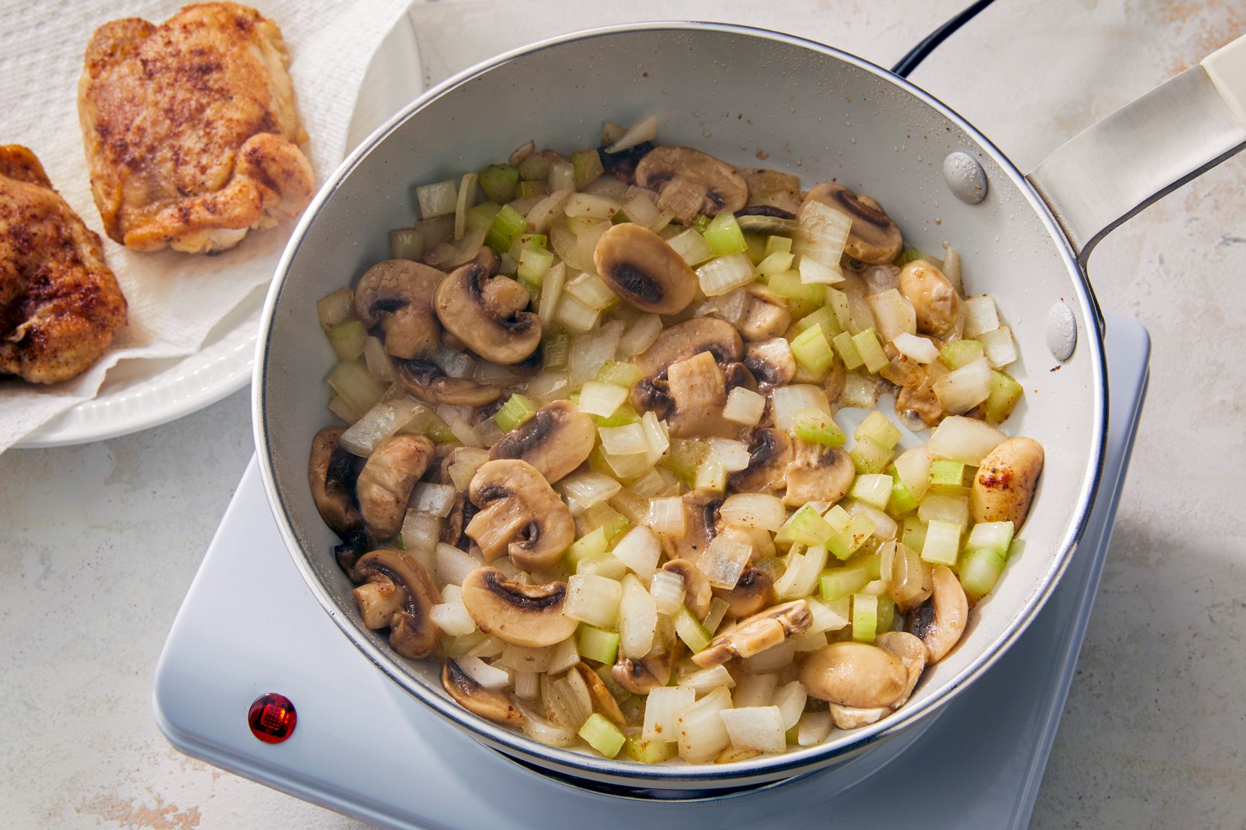 overhead shot; white background; Removed chicken set aside; leaving renderings and now added mushrooms onion and celery heat until soft