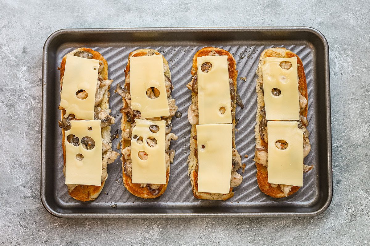 Assembling chicken and Swiss cheese subs on toasted buns.