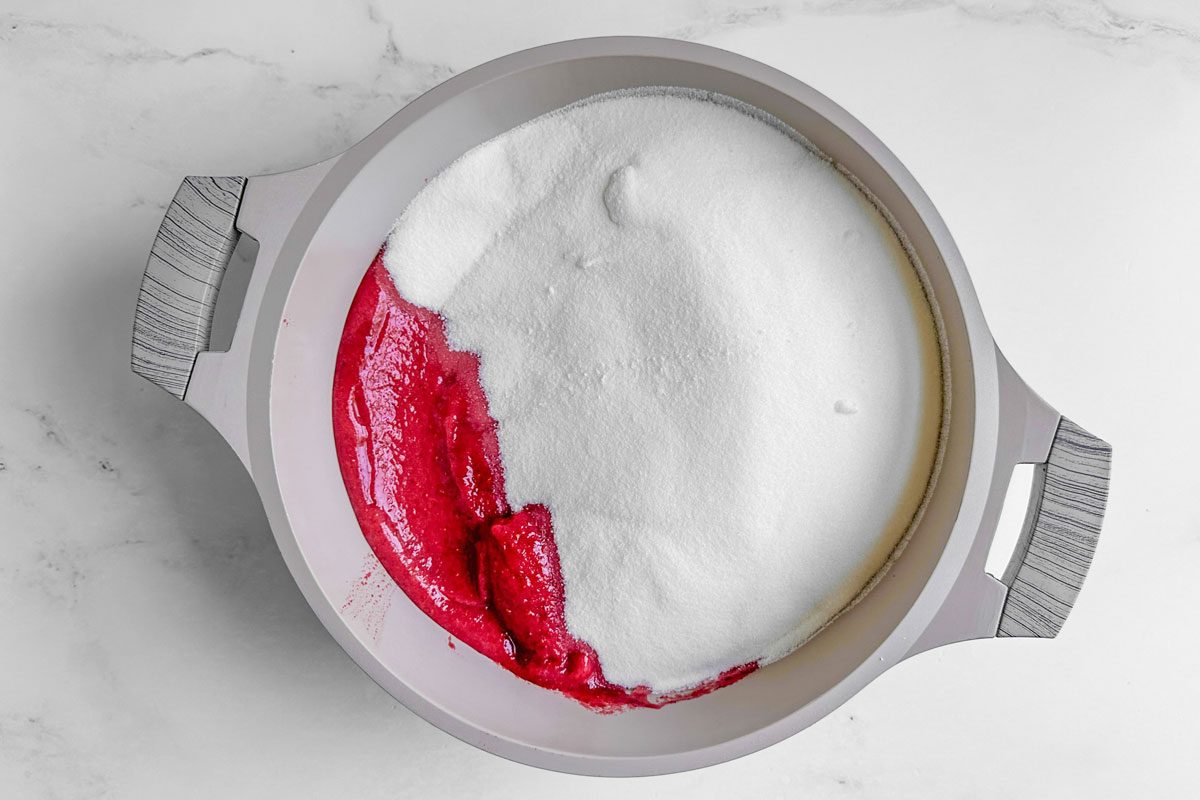 Sugar and pureed berries for Taste of Home Christmas Jam in a Dutch oven on a marble surface