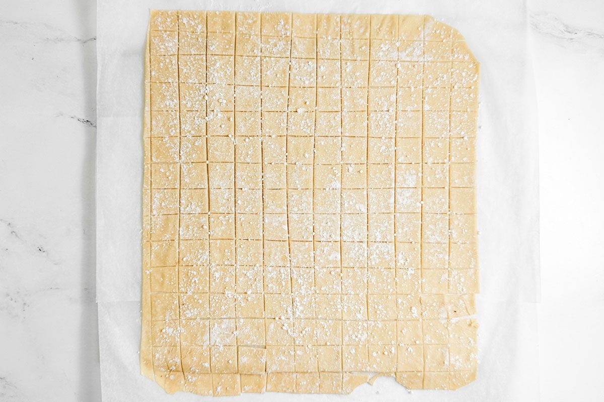 Dough squares for Taste of Home Copycat Cracker Barrel Chicken and Dumplings on parchment paper on a marble surface