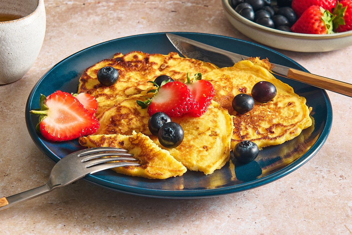 Closeup shot of cottage cheese pancakes topped with berries, being eaten with a fork