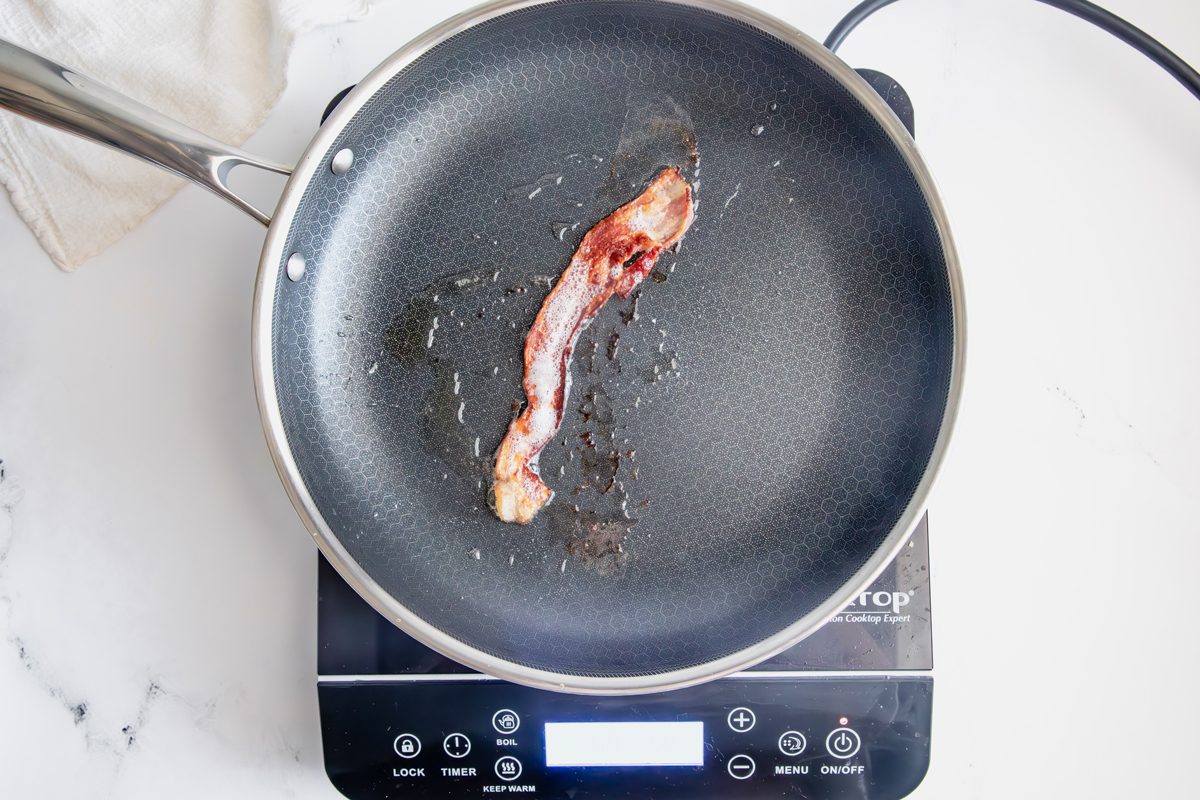 Cooked bacon in a Hexclad pan with bacon grease for Taste of home creamed cabbage on an induction cooktop on a marble surface.