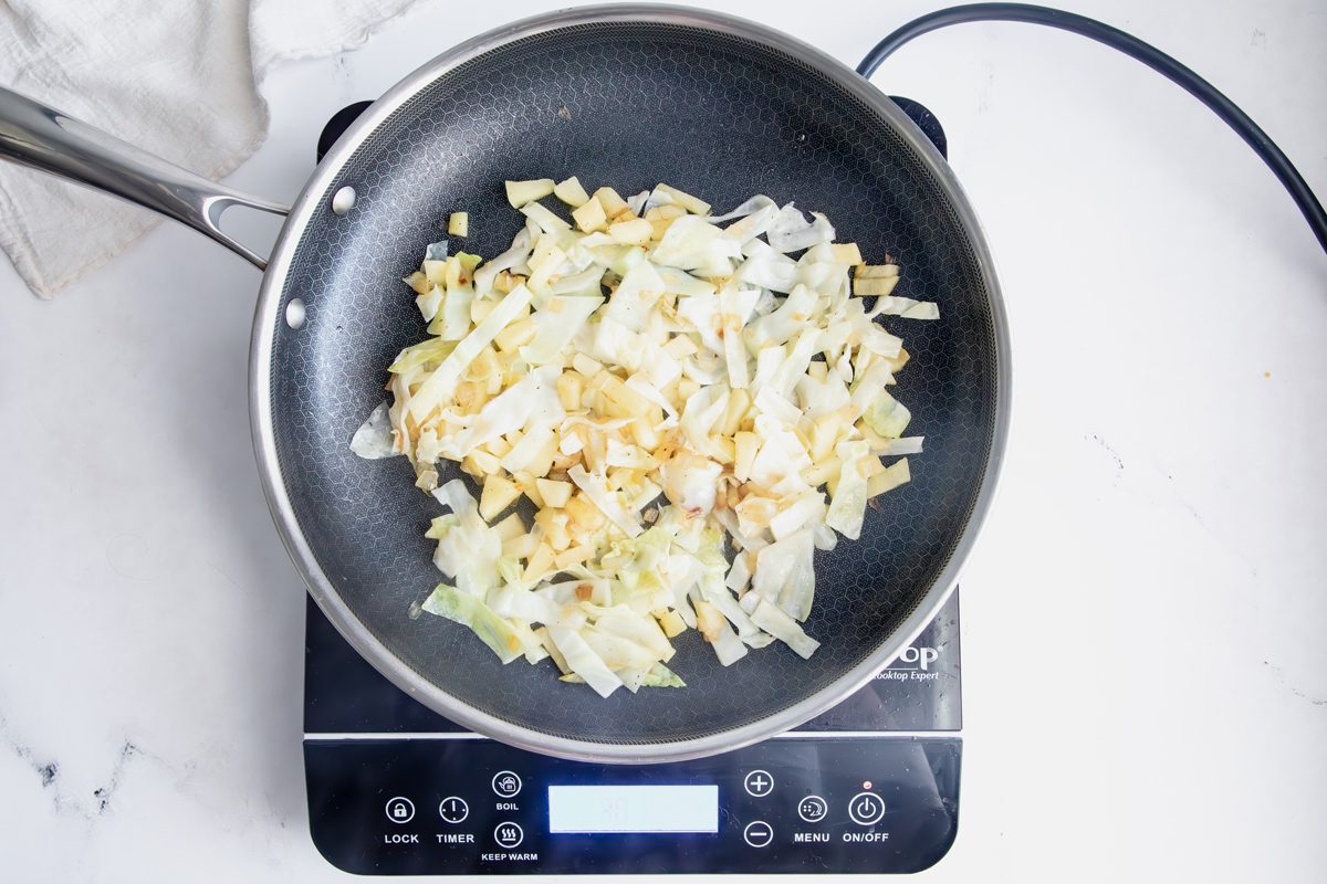Cooking cabbage and apple in a Hexclad pan with bacon grease for Taste of home creamed cabbage on an induction cooktop on a marble surface.