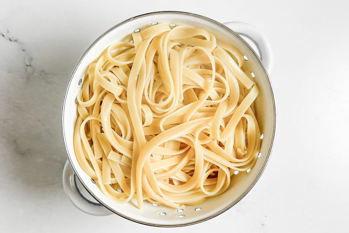 Drained fettucine for Taste of Home Creamy Lemon Pasta in a white colander on a marble surface