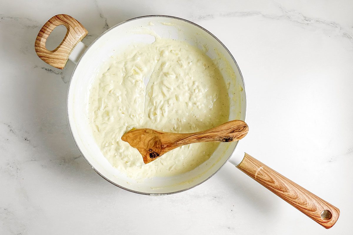 Cream sauce for Taste of Home Creamy Lemon Pasta in a white skillet with wooden spoon on a marble surface