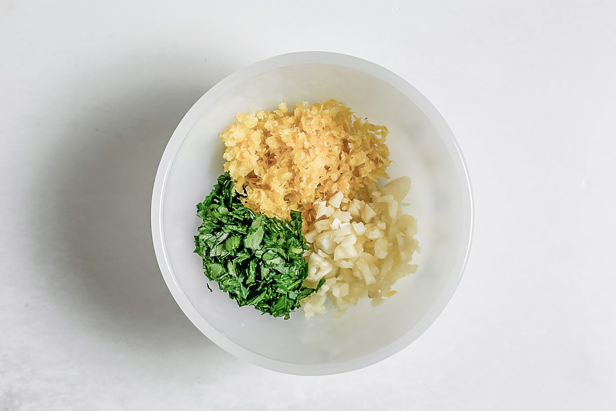 Parsley, lemon zest and minced garlic for Taste of Home Creamy Lemon Pasta iin a white bowl on a marble surface