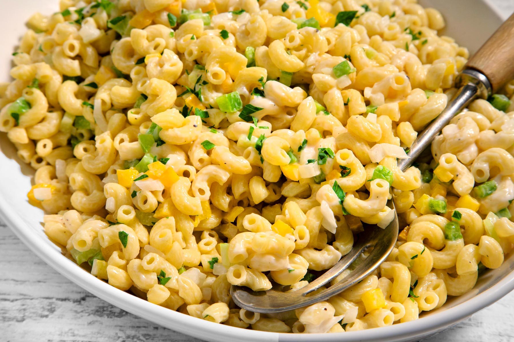 3/4th shot; close shot; wooden textured background; Creamy Macaroni Salad in a oval plate with spoon