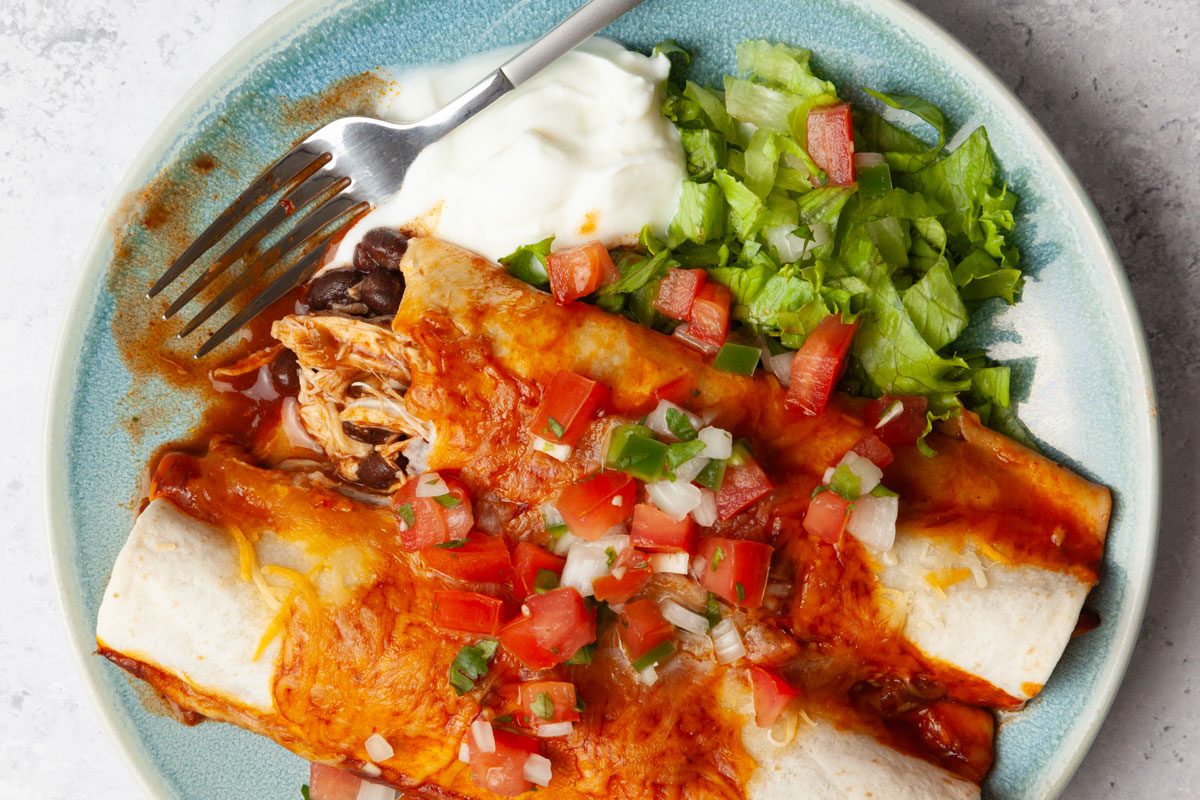 Close up of one servig of Taste of Home Crock-Pot Chicken Enchiladas garnished with pice de gallo, lettuce and sour cream.