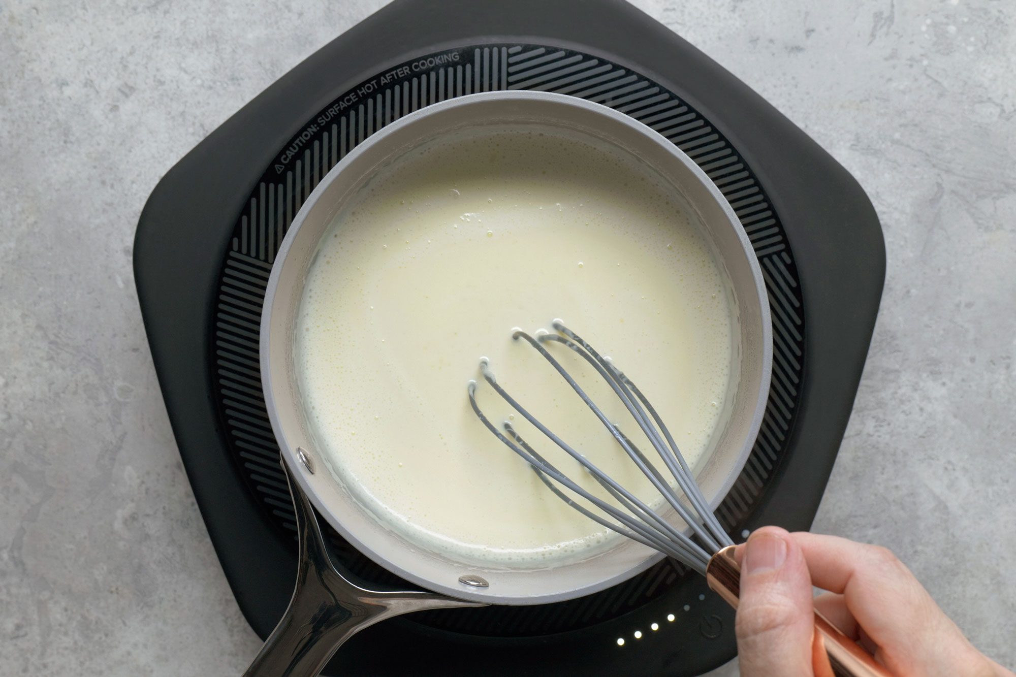 Stirring cream in a large saucepan using a whisker